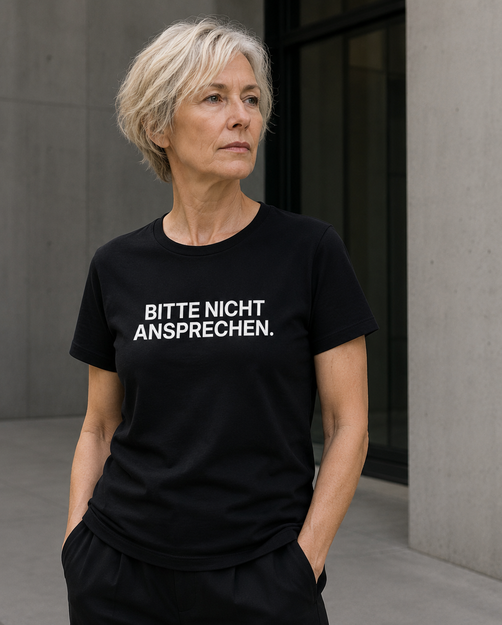 Mature man wearing black BITTE NICHT ANSPRECHEN statement shirt in calm architectural setting.