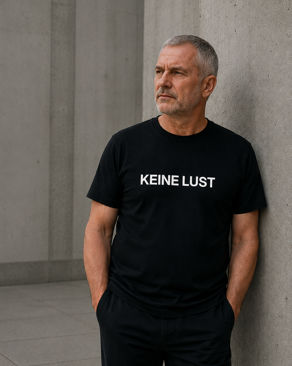 Mature woman wearing black KEINE LUST statement shirt in minimalist concrete setting.