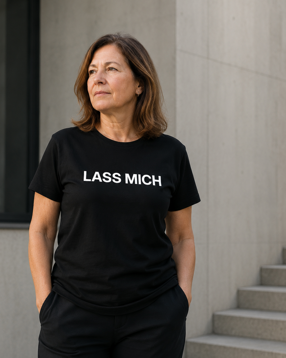 Mature person wearing black LASS MICH statement shirt in clean neutral light.